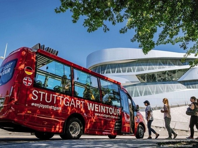 Roter Bus der 'Stuttgart Weintour' vor dem modernen Mercedes-Benz Museum in Stuttgart, umgeben von Passanten und B&auml;umen., &copy; SMG, Thomas Niederm&uuml;ller