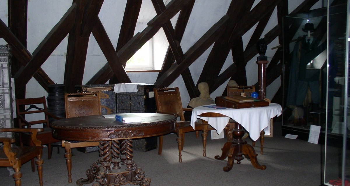 Ein Museumsraum mit antiken Möbeln, darunter runde Tische und Stühle. Sichtbare Holzbalkenstruktur an den Wänden und ein kleines Fenster., © Land der 1000 Hügel - Kraichgau-Stromberg Ein Museumsraum mit antiken Möbeln, darunter runde Tische und Stühle. Sichtbare Holzbalkenstruktur an den Wänden und ein kleines Fenster., © Land der 1000 Hügel - Kraichgau-Stromberg