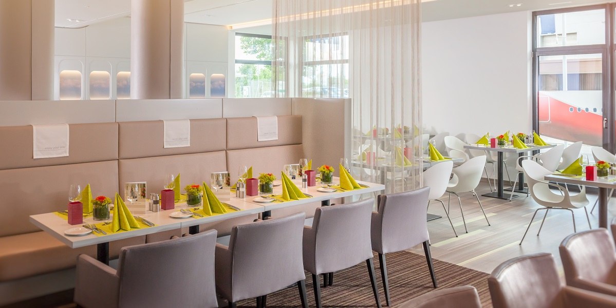 Modernes Restaurant mit eleganter Einrichtung, gedeckten Tischen mit grünen Servietten und stilvollen Stühlen. Helle, freundliche Atmosphäre., © Essential by Dorint