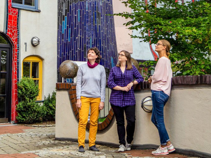 Drei Frauen stehen vor einem farbenfrohen Gebäude im Hundertwasser-Stil in Plochingen. Sie schauen nach oben und wirken interessiert., © PlochingenInfo Drei Frauen stehen vor einem farbenfrohen Gebäude im Hundertwasser-Stil in Plochingen. Sie schauen nach oben und wirken interessiert., © PlochingenInfo