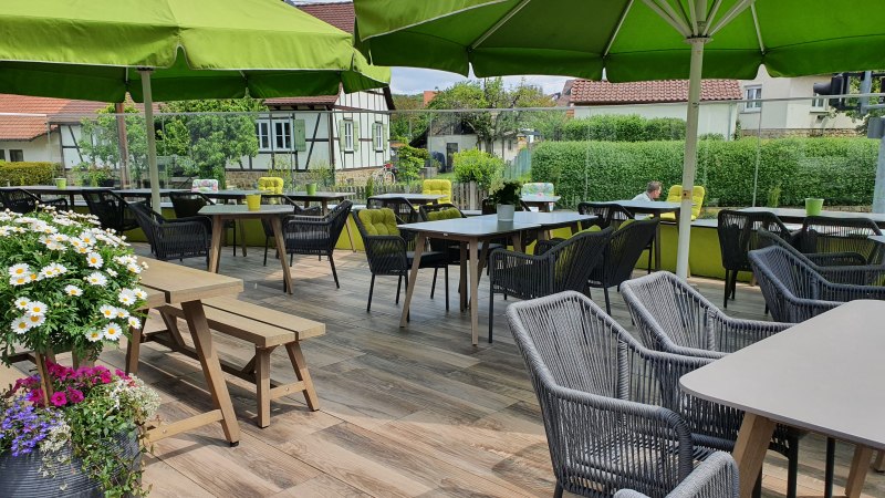 Gemütliche Terrasse eines Landgasthofs mit grünen Sonnenschirmen, Holztischen und Stühlen. Blumen schmücken den Bereich, im Hintergrund Fachwerkhäuser., © Landgasthof Linde Gemütliche Terrasse eines Landgasthofs mit grünen Sonnenschirmen, Holztischen und Stühlen. Blumen schmücken den Bereich, im Hintergrund Fachwerkhäuser., © Landgasthof Linde
