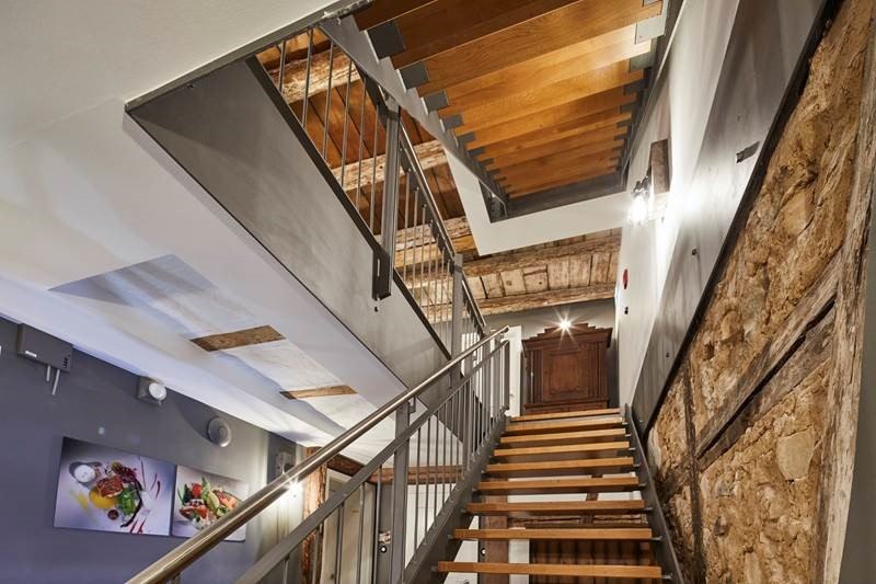 Treppenhaus mit modernen Holzstufen, Metallgeländer und rustikalen Steinwänden. An der Wand hängen Bilder von Speisen., © Hotel Restaurant Bachofer Treppenhaus mit modernen Holzstufen, Metallgeländer und rustikalen Steinwänden. An der Wand hängen Bilder von Speisen., © Hotel Restaurant Bachofer