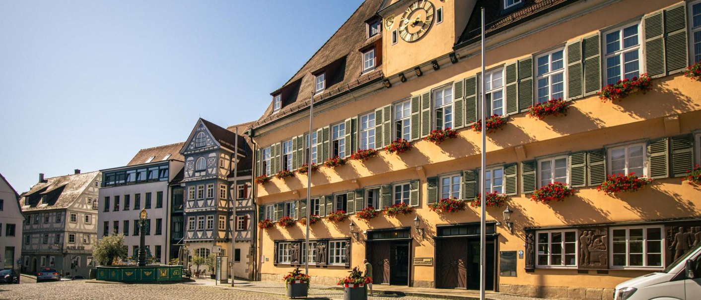 Historische Gebäude am Marktplatz von Nürtingen mit Fachwerk und Blumenschmuck. Die Sonne scheint auf die Fassaden, die mit roten Blumen dekoriert sind., © Stuttgart-Marketing GmbH, Sarah Schmid