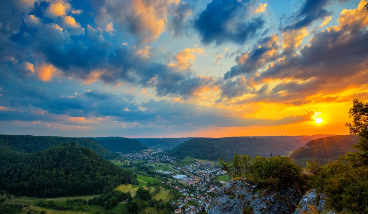 Ein atemberaubender Sonnenuntergang &uuml;ber einer gr&uuml;nen, h&uuml;geligen Landschaft mit einem Dorf im Tal, gesehen vom Oberbergfels., &copy; Landkreis G&ouml;ppingen