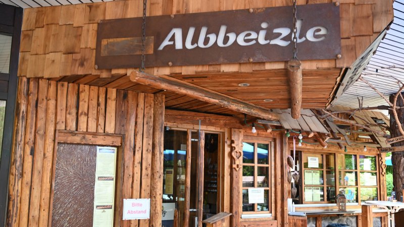Rustikales Gebäude mit Holzverkleidung und dem Schild 'Albbeizle'. Der Eingang ist mit Holzdekor und Schildern gestaltet. Rustikales Gebäude mit Holzverkleidung und dem Schild 'Albbeizle'. Der Eingang ist mit Holzdekor und Schildern gestaltet.