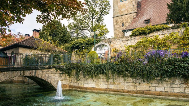 Ein idyllischer Blick auf die Innenstadt von Echterdingen mit einer Steinbrücke, einem Brunnen und einem historischen Turm im Hintergrund., © Stuttgart-Marketing GmbH, Sarah Schmid