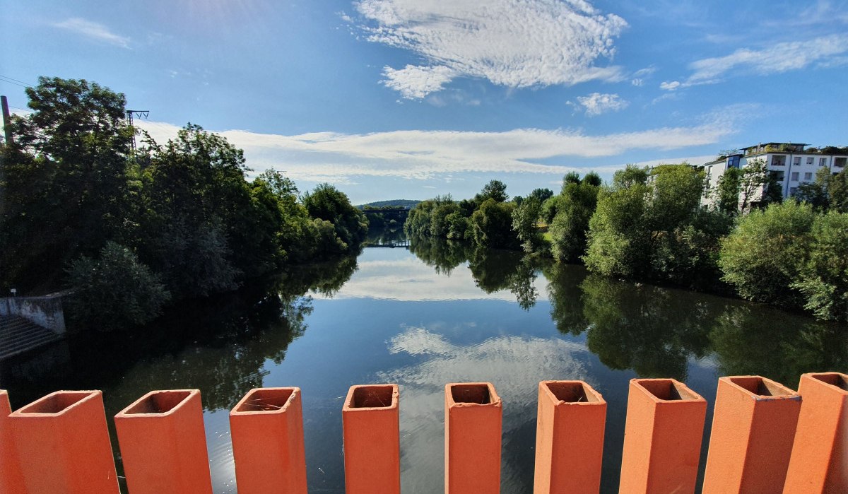 Blick von der Ottosteg-Brücke in Plochingen auf einen ruhigen Fluss, umgeben von Bäumen und Gebäuden, unter einem klaren blauen Himmel., © Kulturamt Plochingen Blick von der Ottosteg-Brücke in Plochingen auf einen ruhigen Fluss, umgeben von Bäumen und Gebäuden, unter einem klaren blauen Himmel., © Kulturamt Plochingen