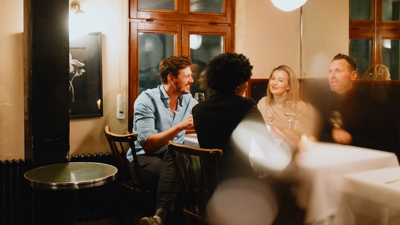Vier Personen sitzen in einer gemütlichen Weinstube, unterhalten sich und genießen Wein. Die Atmosphäre ist warm und einladend., © Stuttgart-Marketing GmbH, Alwin Maigler