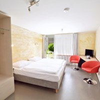 Helles Zimmer mit Doppelbett, zwei roten Stühlen, Schreibtisch, Fernseher und großem Fenster mit Blick ins Grüne., © Abalon Hotel Ideal