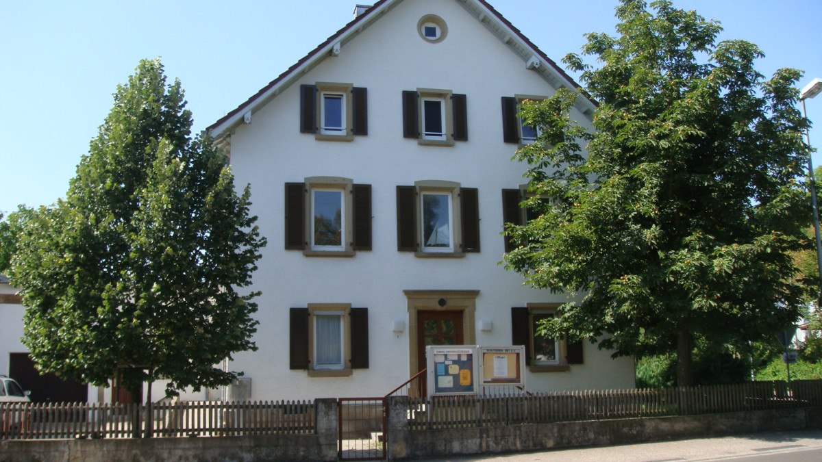 Ein weißes Haus mit braunen Fensterläden, umgeben von Bäumen und einem Holzzaun. Der Himmel ist klar und blau., © Land der 1000 Hügel - Kraichgau-Stromberg