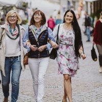 Drei Frauen gehen lachend Arm in Arm durch eine belebte Fußgängerzone in Schwäbisch Hall. Im Hintergrund sind weitere Passanten und Geschäfte zu sehen., © Nico Kurth