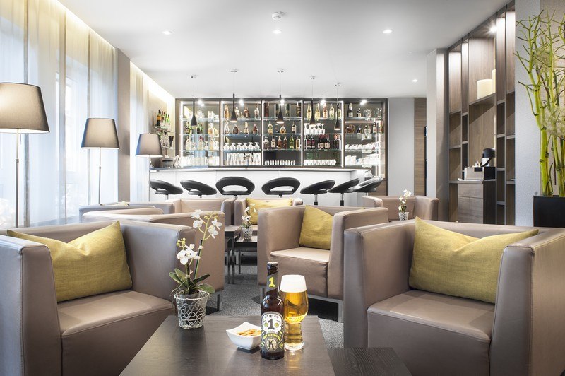 Moderne Bar/Lobby mit bequemen Sesseln, Barhockern und gut bestückter Theke. Einladende Atmosphäre mit Getränken und Snacks auf den Tischen., © TOMAS