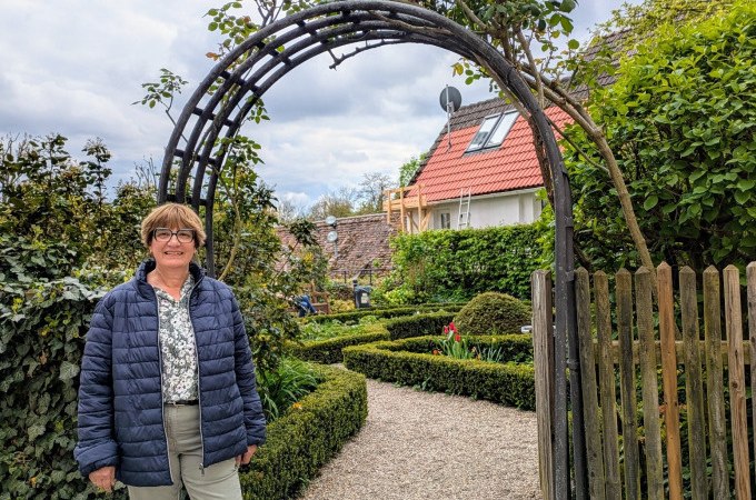Frau vor einem Gartenbogen, umgeben von gepflegtem Garten mit Hecken und Blumen. Im Hintergrund ein Haus mit rotem Dach., © WTM GmbH Waiblingen Frau vor einem Gartenbogen, umgeben von gepflegtem Garten mit Hecken und Blumen. Im Hintergrund ein Haus mit rotem Dach., © WTM GmbH Waiblingen
