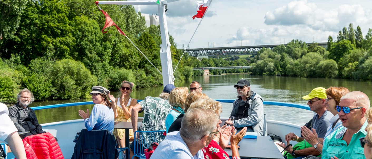Menschen genie&szlig;en eine Bootsfahrt auf dem Neckar. Sie sitzen auf dem Deck, umgeben von gr&uuml;ner Landschaft und unterhalten sich fr&ouml;hlich., &copy; all copyrights are reserved by maks richter