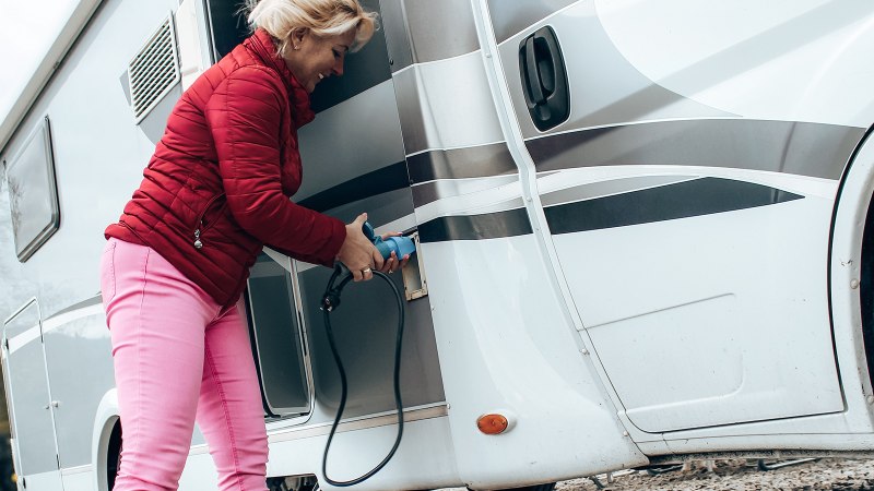 Eine Frau in roter Jacke und pinker Hose schließt ein Wohnmobil an eine Stromquelle an. Sie hält ein blaues Kabel in der Hand., © Erlebnisregion Schwäbischer Albtrauf e. V.