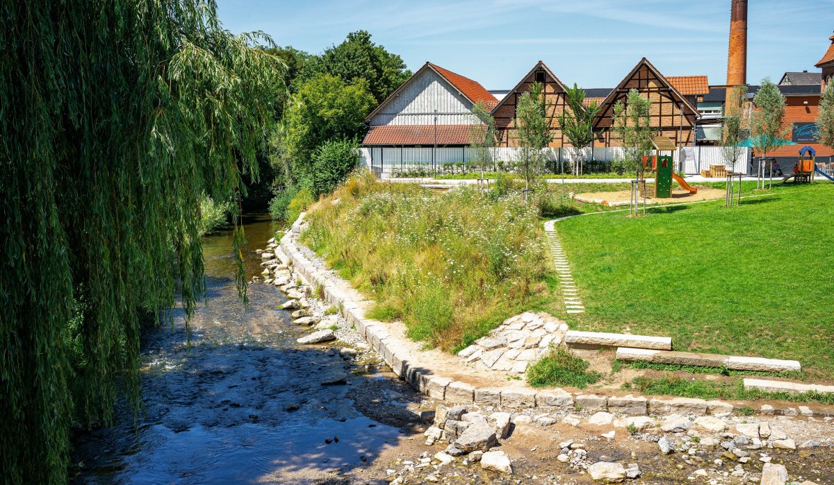 Ein Fluss fließt an einem Park mit Spielplatz und Fachwerkhäusern vorbei. Im Hintergrund ist ein hoher Schornstein zu sehen., © Remstal Tourismus e.V. Ein Fluss fließt an einem Park mit Spielplatz und Fachwerkhäusern vorbei. Im Hintergrund ist ein hoher Schornstein zu sehen., © Remstal Tourismus e.V.