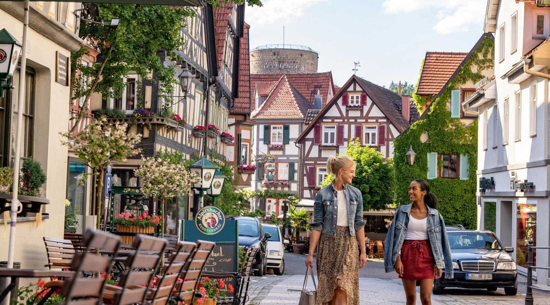 Blick die Kirchstraße mit ihren Fachwerkhäusern entlang auf den gemauerten Waldhornturm. Zwei Frauen flanieren durch die Straße., © SMG, Martina Denker