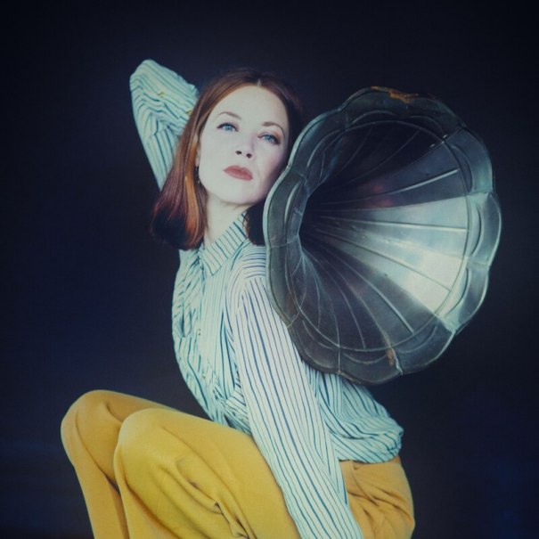 Frau in gestreiftem Hemd und gelber Hose posiert mit einem Grammophontrichter vor dunklem Hintergrund., © Mauerwerk GmbH Frau in gestreiftem Hemd und gelber Hose posiert mit einem Grammophontrichter vor dunklem Hintergrund., © Mauerwerk GmbH