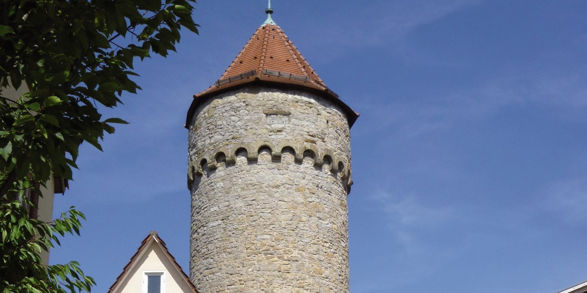 Der Haspelturm in Vaihingen an der Enz mit rundem Steinturm und spitzem Dach, umgeben von Bäumen, vor blauem Himmel., © Stadt Vaihingen an der Enz Der Haspelturm in Vaihingen an der Enz mit rundem Steinturm und spitzem Dach, umgeben von Bäumen, vor blauem Himmel., © Stadt Vaihingen an der Enz