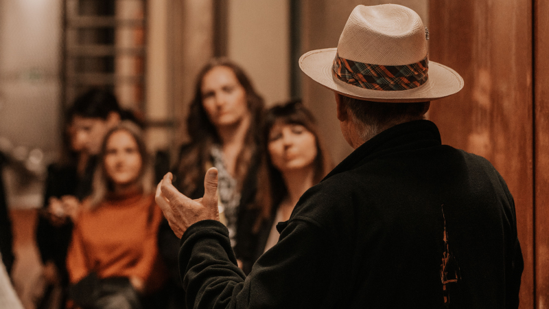 Ein Mann mit Hut erkl&auml;rt einer Gruppe von Menschen etwas in einem Weinkeller. Die Zuh&ouml;rer wirken interessiert., &copy; Fellbacher Weing&auml;rtner eG