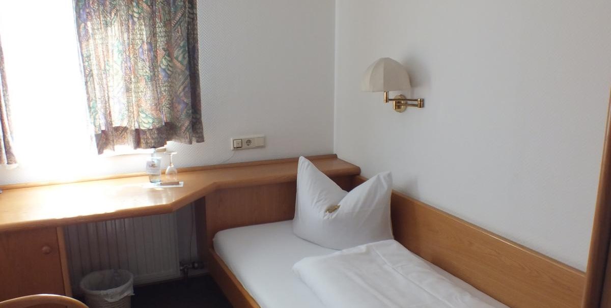 Ein kleines Einzelzimmer mit einem Bett, einem Schreibtisch, einem Stuhl und einem Fenster mit Vorhängen., © Gasthof zum Bären