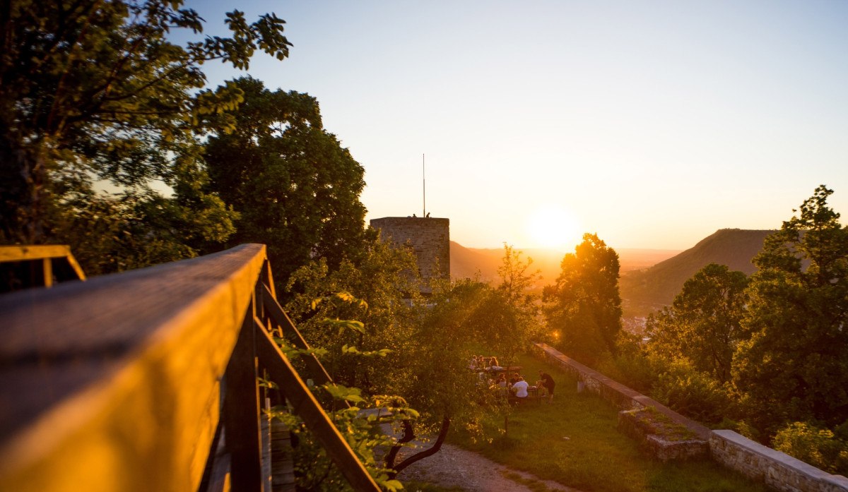Die Burgruine Helfenstein bei Sonnenuntergang, umgeben von B&auml;umen. Menschen sitzen auf einer Wiese und genie&szlig;en die Aussicht., &copy; Landkreis G&ouml;ppingen