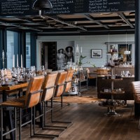 Stilvolles Restaurant mit Holzböden, Ledersesseln und gedeckten Tischen. An der Wand eine Tafel mit Weinauswahl. Elegante Atmosphäre., © Check Inn Restaurant