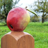 Eine große Apfelskulptur auf einem Holzpfosten vor einer grünen Wiese mit Bäumen im Hintergrund. Eine große Apfelskulptur auf einem Holzpfosten vor einer grünen Wiese mit Bäumen im Hintergrund.