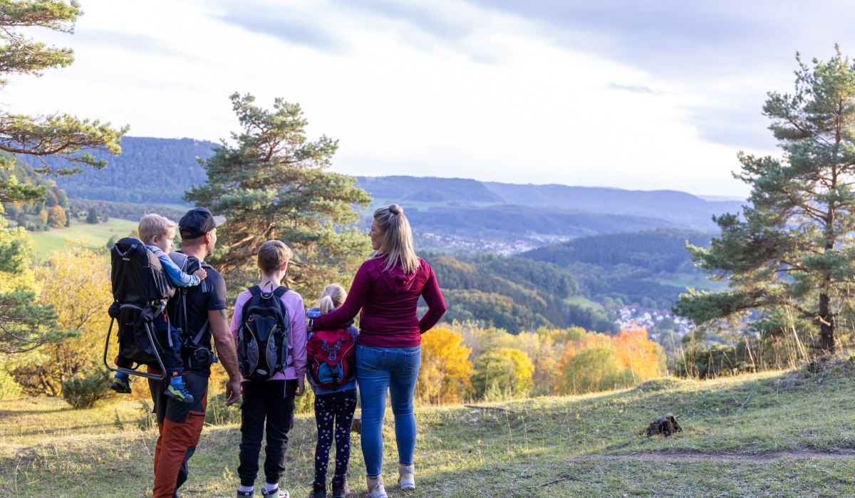Eine Familie steht auf einem Hügel und blickt auf eine malerische Landschaft mit Wäldern und Hügeln. Die Sonne scheint durch die Bäume., © Foto Thomas Zehnder