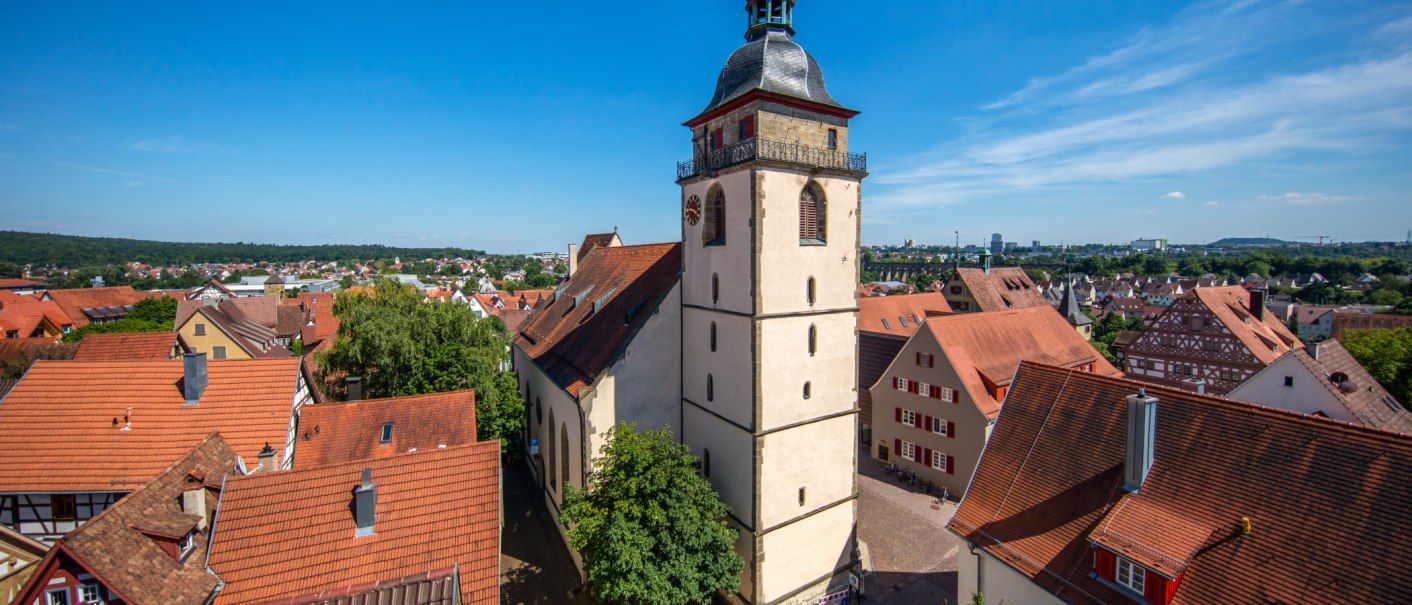 Die Evangelische Stadtkirche Bietigheim-Bissingen ragt über die roten Dächer der Altstadt, umgeben von Bäumen und unter einem klaren blauen Himmel., © SMG, Achim Mende Die Evangelische Stadtkirche Bietigheim-Bissingen ragt über die roten Dächer der Altstadt, umgeben von Bäumen und unter einem klaren blauen Himmel., © SMG, Achim Mende