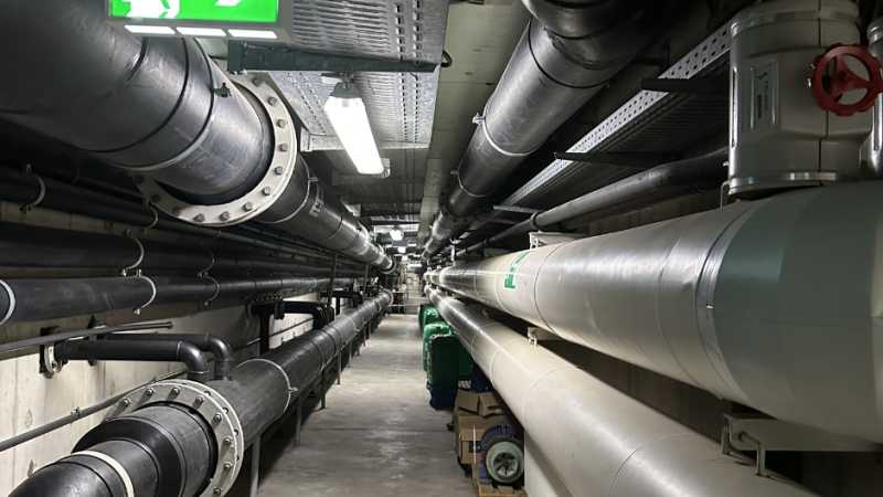 Ein unterirdischer Technikgang mit gro&szlig;en Rohren und einem leuchtenden Notausgangsschild an der Decke., &copy; Stadtwerke Ludwigsburg-Kornwestheim GmbH