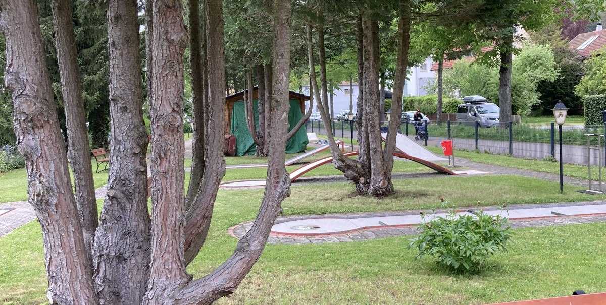 Minigolfplatz in Bad Urach mit Bäumen, einer Holzbank im Vordergrund und Minigolfbahnen im Hintergrund.