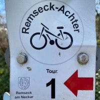 Schild mit 'Remseck-Achter', Fahrradsymbol, 'Tour 1' und rotem Pfeil nach links. Unten das Wappen von Remseck am Neckar.