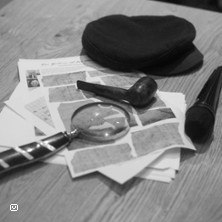 Ein Tisch mit einer Lupe, Pfeife, Mikrofon und Hut auf Papieren, die an Detektivarbeit erinnern., &copy; links im Bild