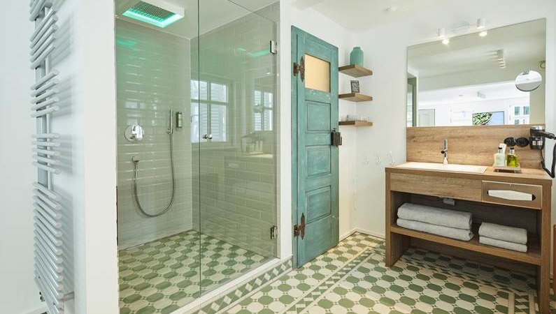 Modernes Badezimmer mit Glasdusche, grünem Fliesenboden, Holzwaschtisch und türkisfarbener Tür. Handtücher und Pflegeprodukte sind bereitgestellt., © Hotel Restaurant Bachofer Modernes Badezimmer mit Glasdusche, grünem Fliesenboden, Holzwaschtisch und türkisfarbener Tür. Handtücher und Pflegeprodukte sind bereitgestellt., © Hotel Restaurant Bachofer