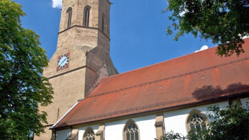 Kirche mit hohem Turm und roten Dachziegeln, umgeben von B&auml;umen. Der Himmel ist blau mit wenigen Wolken., &copy; Waiblingen - Stuttgart-Marketing GmbH