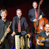 Eine Jazzband mit Saxophon, Akkordeon, Kontrabass und Gitarre posiert auf einer Bühne. Die Musiker tragen dunkle Anzüge und lächeln in die Kamera., © Stadt Murrhardt