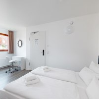 Helles Doppelzimmer mit zwei Betten, einem Schreibtisch und Stuhl. Ein Fenster mit Vorhang und ein Wandspiegel sind sichtbar., &copy; Hotel Olgaeck
