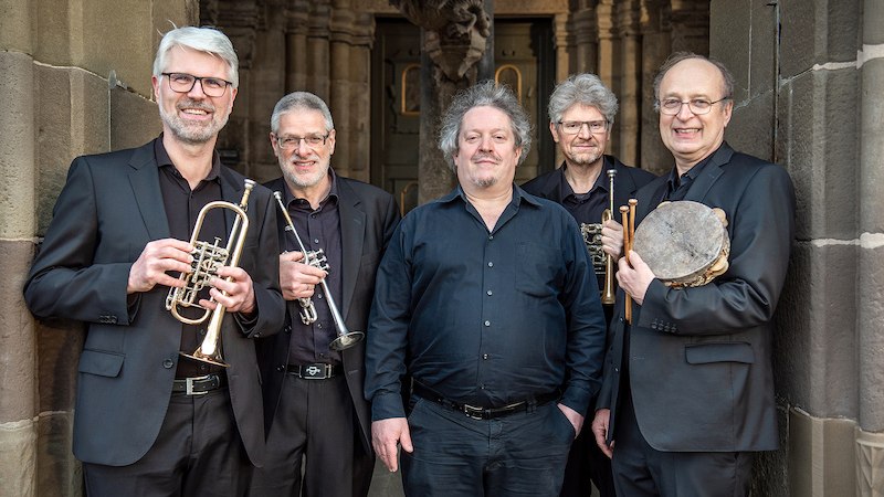 Fünf Männer in schwarzen Anzügen stehen vor einem historischen Gebäude. Zwei halten Trompeten, einer eine Trommel. Sie lächeln in die Kamera., © Konzertbüro Joachim Jung Fünf Männer in schwarzen Anzügen stehen vor einem historischen Gebäude. Zwei halten Trompeten, einer eine Trommel. Sie lächeln in die Kamera., © Konzertbüro Joachim Jung