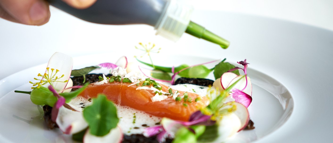 Ein Gourmetgericht mit Lachs, essbaren Blumen und grüner Sauce auf einem weißen Teller, kunstvoll angerichtet., © Stuttgart-Marketing GmbH, Annette Sandner Ein Gourmetgericht mit Lachs, essbaren Blumen und grüner Sauce auf einem weißen Teller, kunstvoll angerichtet., © Stuttgart-Marketing GmbH, Annette Sandner