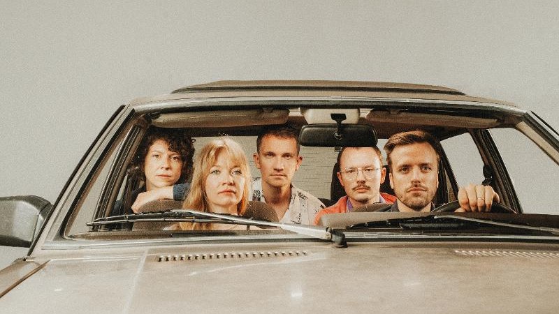 Fünf Personen sitzen in einem Auto und blicken ernst nach vorne. Die Szene wirkt inszeniert und künstlerisch., © SKS Michael Russ GmbH Fünf Personen sitzen in einem Auto und blicken ernst nach vorne. Die Szene wirkt inszeniert und künstlerisch., © SKS Michael Russ GmbH