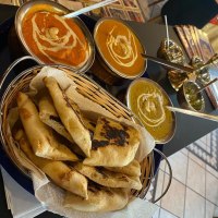 Drei Schalen mit indischen Currys und ein Korb mit Naan-Brot auf einem Tisch in einem Restaurant., © Taj Mahal Bad Urach