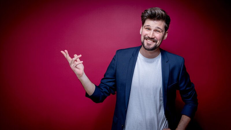 Mann in blauem Sakko und weißem T-Shirt lächelt vor rotem Hintergrund., © Stadt Leinfelden-Echterdingen, Kulturamt