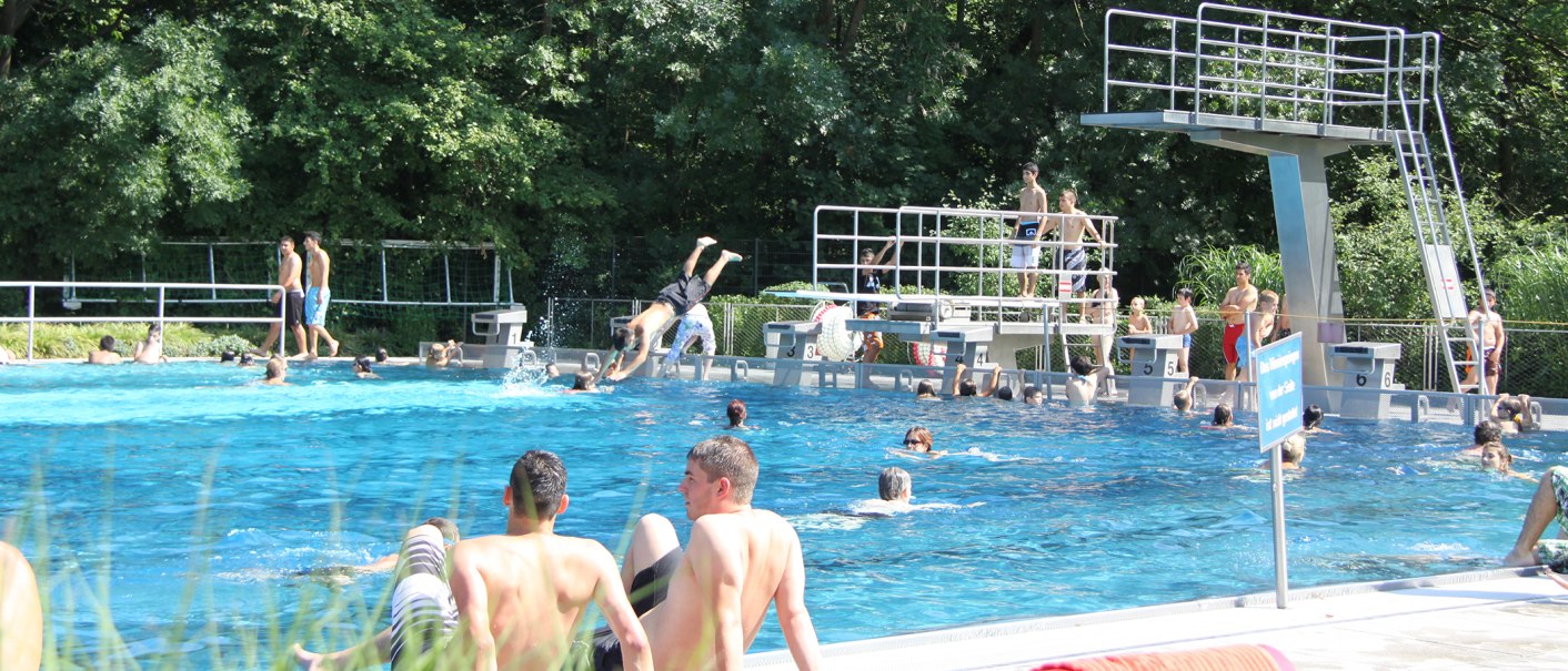 Menschen genießen das Freibad Kirchheim unter Teck. Einige schwimmen, andere springen vom Sprungturm. Im Hintergrund sind Bäume zu sehen., © Torsten Wenzler
