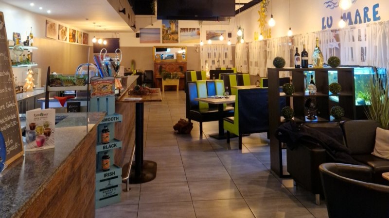 Ein modernes Restaurant mit grünen Stühlen, Holztischen und dekorativen Pflanzen. An der Wand steht "LU MARE". Die Beleuchtung ist warm und einladend., © Pizzeria Salento Ein modernes Restaurant mit grünen Stühlen, Holztischen und dekorativen Pflanzen. An der Wand steht "LU MARE". Die Beleuchtung ist warm und einladend., © Pizzeria Salento