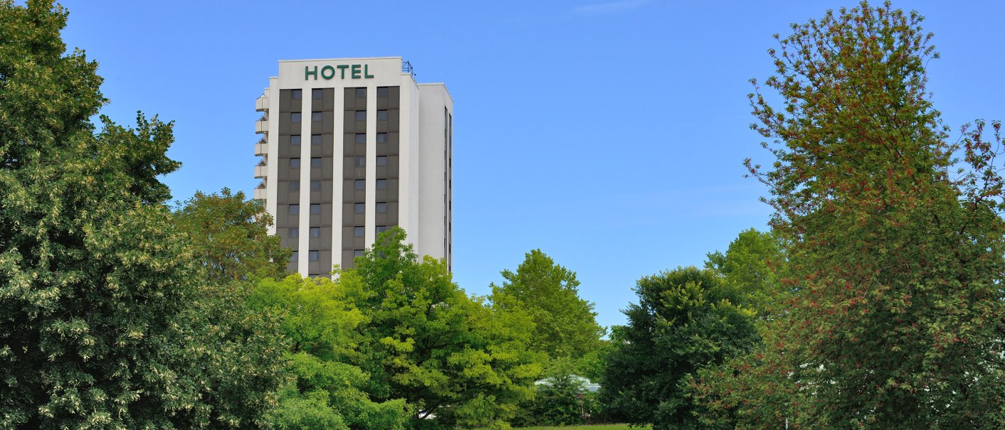 Hotelgeb&auml;ude hinter B&auml;umen in einem Park, blauer Himmel., &copy; AMBER HOTEL Leonberg / Stuttgart