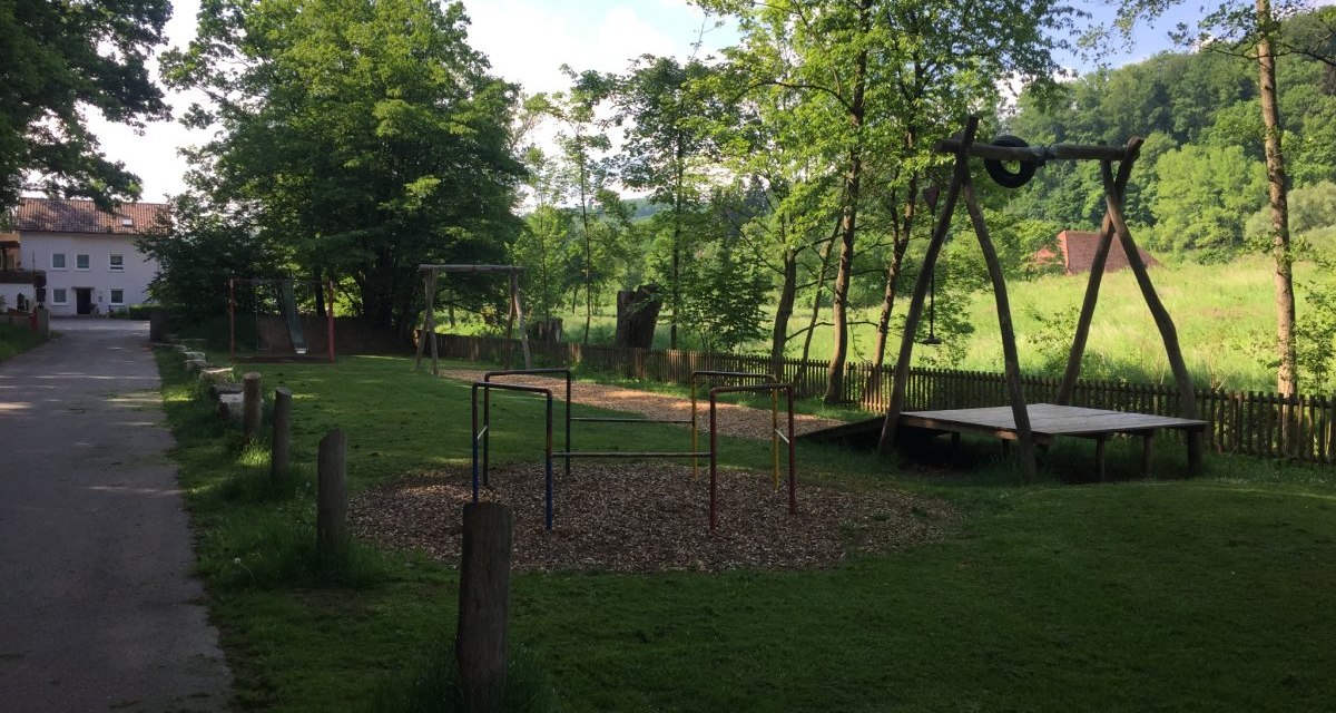 Ein ruhiger Spielplatz mit Schaukeln und Klettergerüst, umgeben von Bäumen und Wiesen. Ein Weg führt am Spielplatz vorbei., © www.pro-cycl.de Ein ruhiger Spielplatz mit Schaukeln und Klettergerüst, umgeben von Bäumen und Wiesen. Ein Weg führt am Spielplatz vorbei., © www.pro-cycl.de