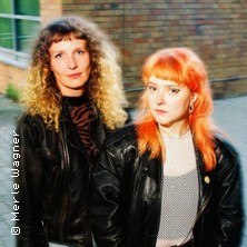 Zwei Frauen mit Lederjacken und unterschiedlichen Haarfarben stehen vor einer Backsteinmauer., © links im Bild