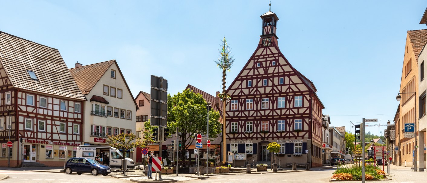 Platz ges&auml;umt von verschiedenen Geb&auml;uden, darunter zwei mit FAchwerkfassaden, in der Platzmitte Baum und Brunnen, &copy; Stadt Gaildorf