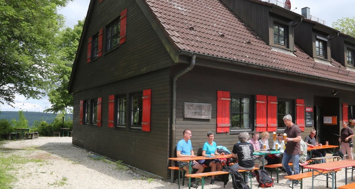 Holzhaus mit roten Fensterläden, Menschen sitzen an Biertischen im Freien. Schild mit "Knörzerhaus" an der Wand. Bäume und Himmel im Hintergrund., © Foto Walter Laible Holzhaus mit roten Fensterläden, Menschen sitzen an Biertischen im Freien. Schild mit "Knörzerhaus" an der Wand. Bäume und Himmel im Hintergrund., © Foto Walter Laible